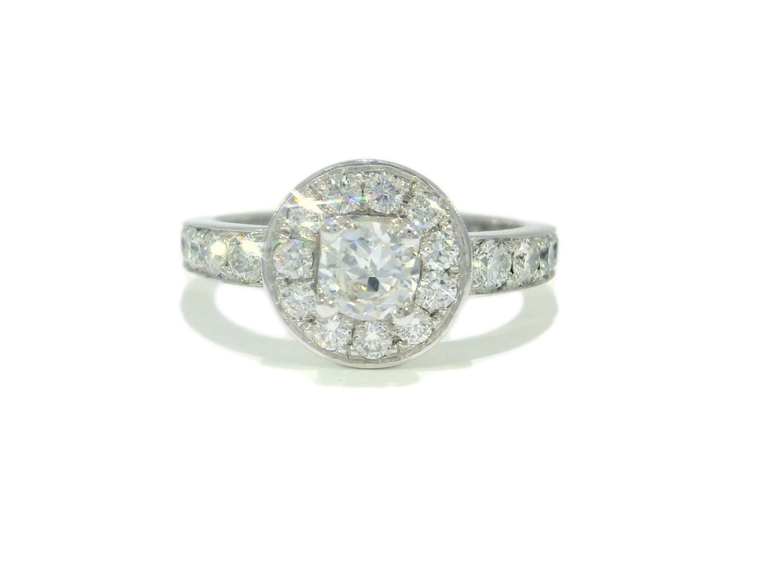 An 18KT white gold engagement ring with a round brilliant cut halo diamond center stone surrounded by smaller diamonds.