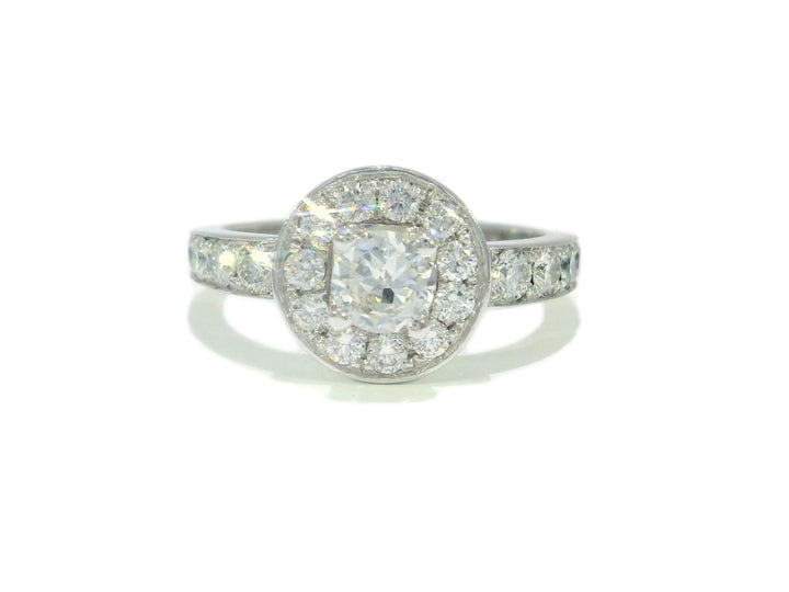 An 18KT white gold engagement ring with a round brilliant cut halo diamond center stone surrounded by smaller diamonds.