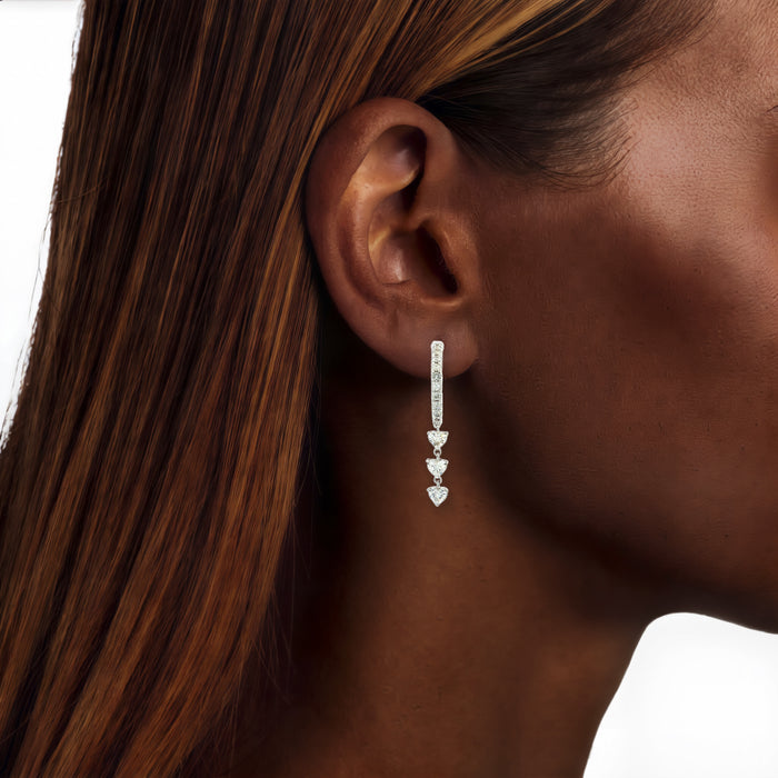 Heart Colorless Nearly Flawless Diamond Dangle Hoop Earrings (⅞ ct. tw.) in 18k White Gold shown on the ear (deep skin tone)