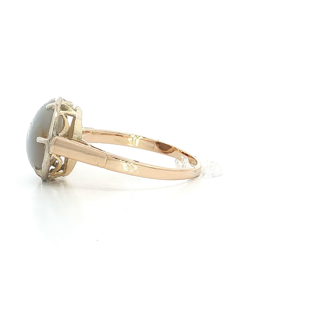 Gold ring with oval grey gemstone cabochon in prong setting, side view