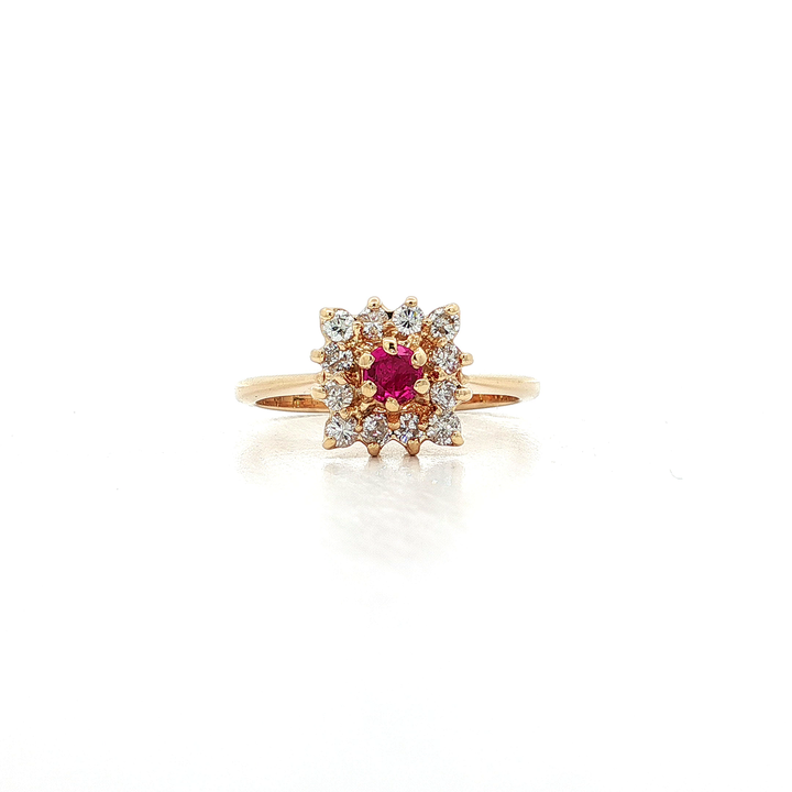 Gold ring with a round red gemstone center, surrounded by a halo of clear diamonds