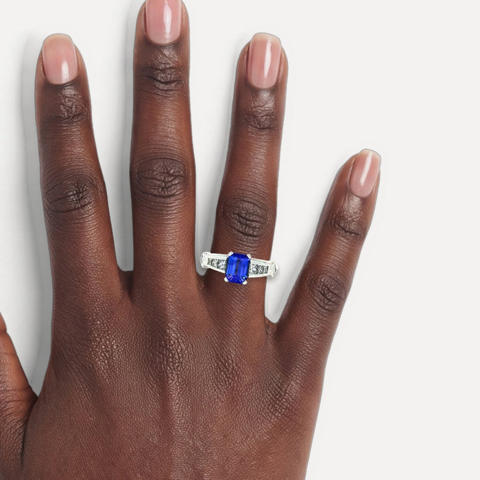Vivid Emerald-Cut Tanzanite Channel-Set Diamond Ring (2 ¼ ct. tw.) in 18k White Gold shown on a hand (deep skin tone)