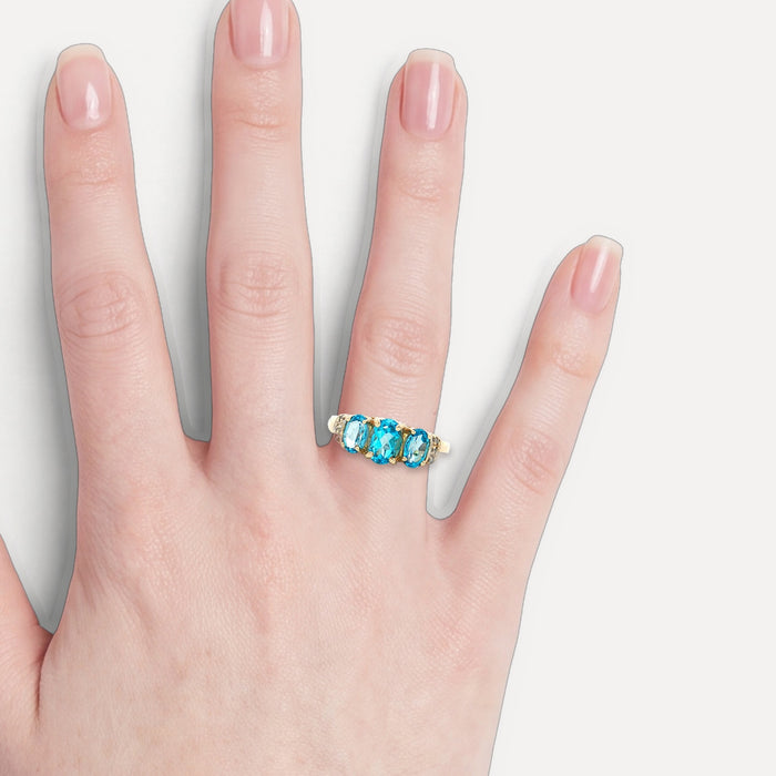 Brilliant London Blue Topaz & Near-Colorless Diamond Past Present Future Three-Stone Ring (1 ⅗ ct. tw.) in 10k Yellow Gold shown on a hand (light skin tone)