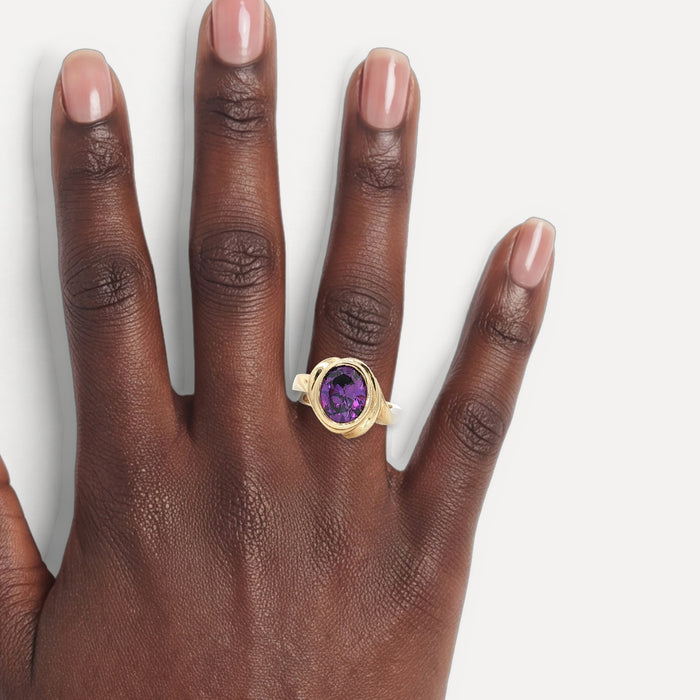 Oval Brilliant Cut Deep Purple Amethyst Bezel-Set Ring (2 ⅙ ct.) in 10k Yellow Gold shown on a hand (deep skin tone)