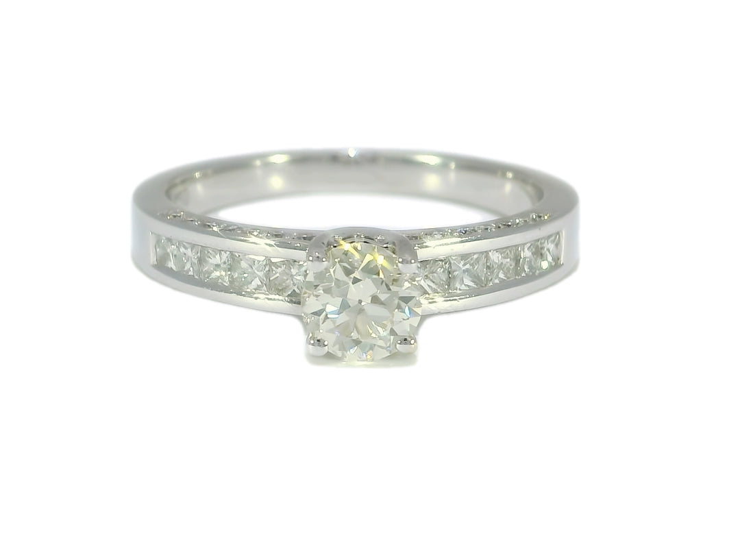 A round diamond engagement ring with smaller diamonds on the band, set in 18KT white gold.