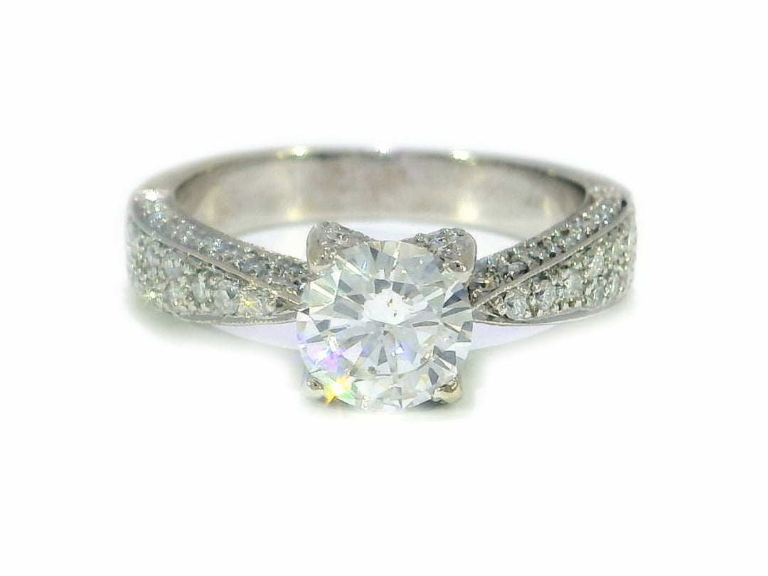 A close-up image of a round brilliant cut diamond engagement ring with a pavé mounting in 14KT white gold.