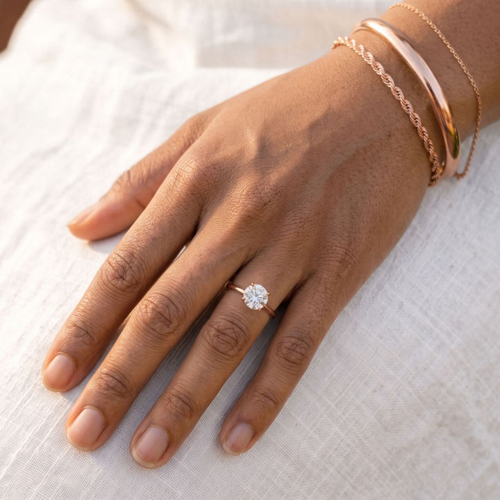 Rose gold stacked bracelets and a round solitaire ring on medium skin