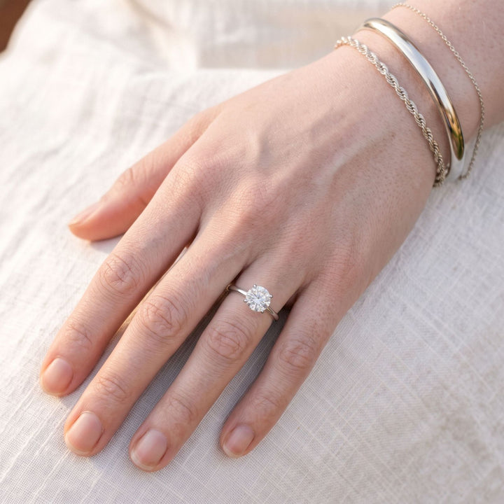 White gold stacked bracelets and a round solitaire ring on fair skin