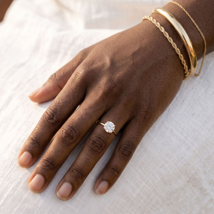 Yellow gold stacked bracelets and a round solitaire ring on deep skin